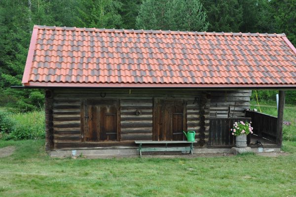 Traditionell timmerstuga med rött tegeltak omgiven av grönska